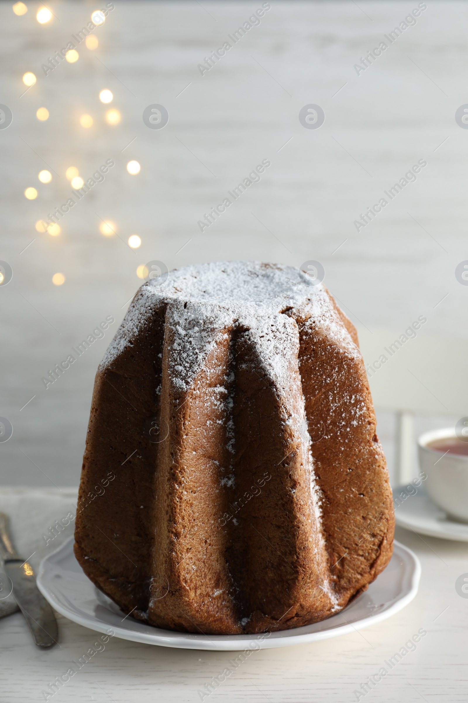 Photo of Delicious Pandoro cake decorated with powdered sugar on white wooden table. Traditional Italian pastry
