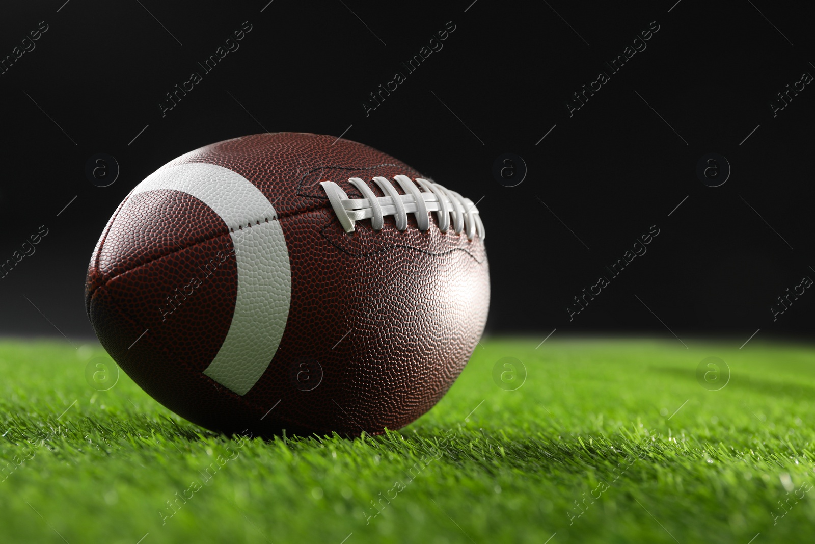 Photo of Rugby ball on green grass against black background, space for text
