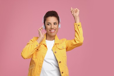Photo of Happy young woman in headphones dancing on pink background