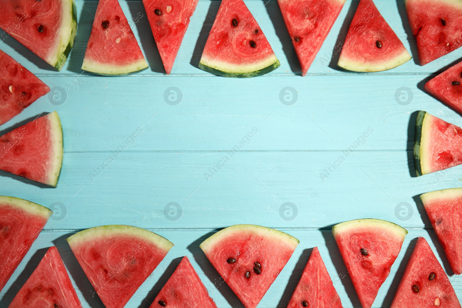 Photo of Frame made with slices of ripe watermelon on light blue wooden table, flat lay. Space for text