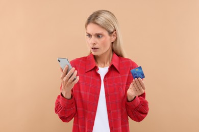 Stressed woman with credit card and smartphone on beige background. Be careful - fraud