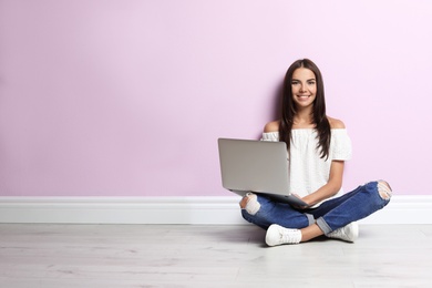 Young woman with modern laptop sitting near color wall