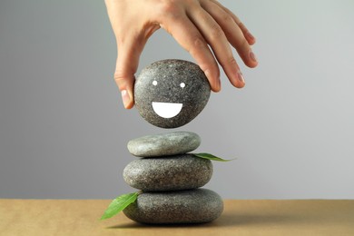 Photo of Woman putting stone drawn happy face onto stack against grey background, closeup. Zen concept