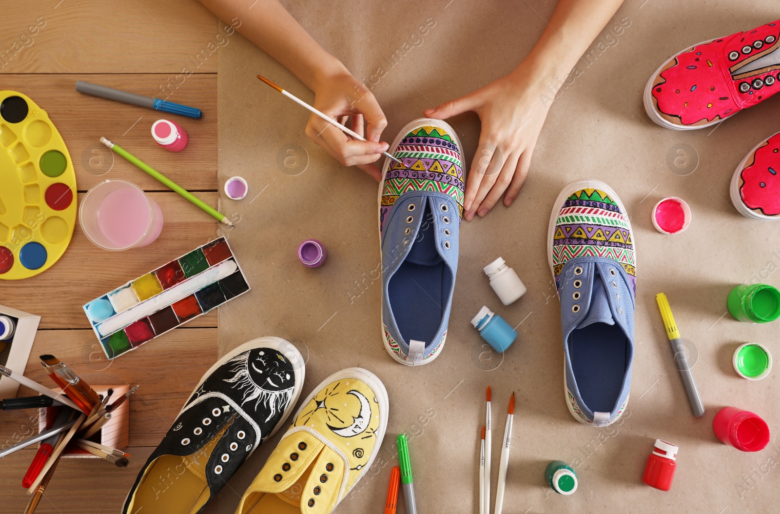 Photo of Woman painting on sneaker at wooden table, top view. Customized shoes