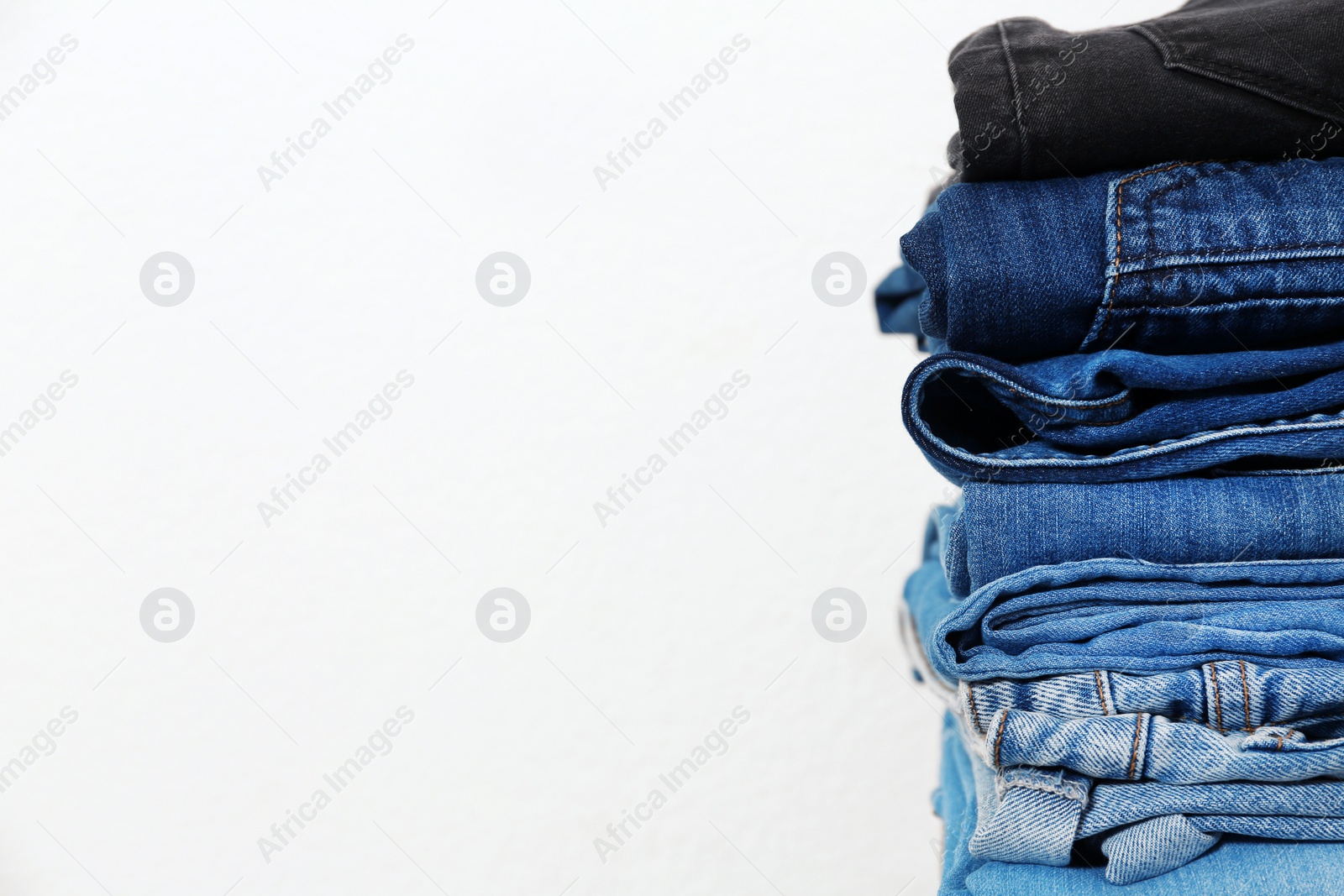 Photo of Stack of different jeans against white background. Space for text