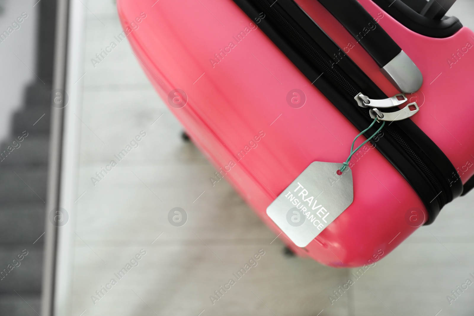 Photo of Stylish suitcase with travel insurance label on blurred background, closeup. Space for text