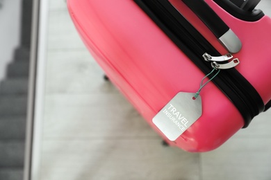 Stylish suitcase with travel insurance label on blurred background, closeup. Space for text