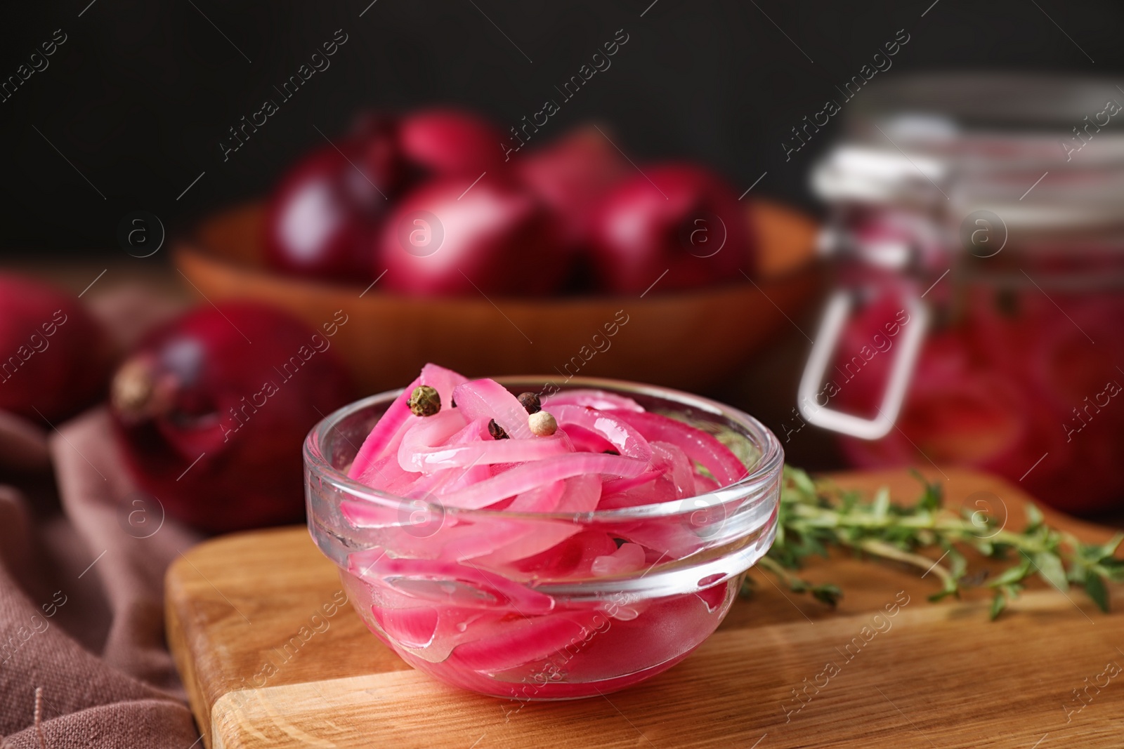 Photo of Bowl with tasty pickled onions on wooden cutting board