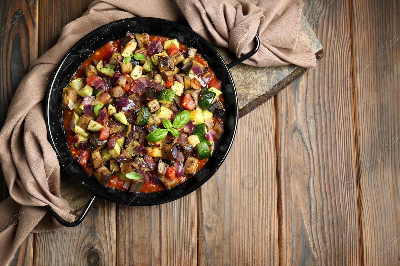 Photo of Delicious ratatouille in baking dish on wooden table, top view. Space for text