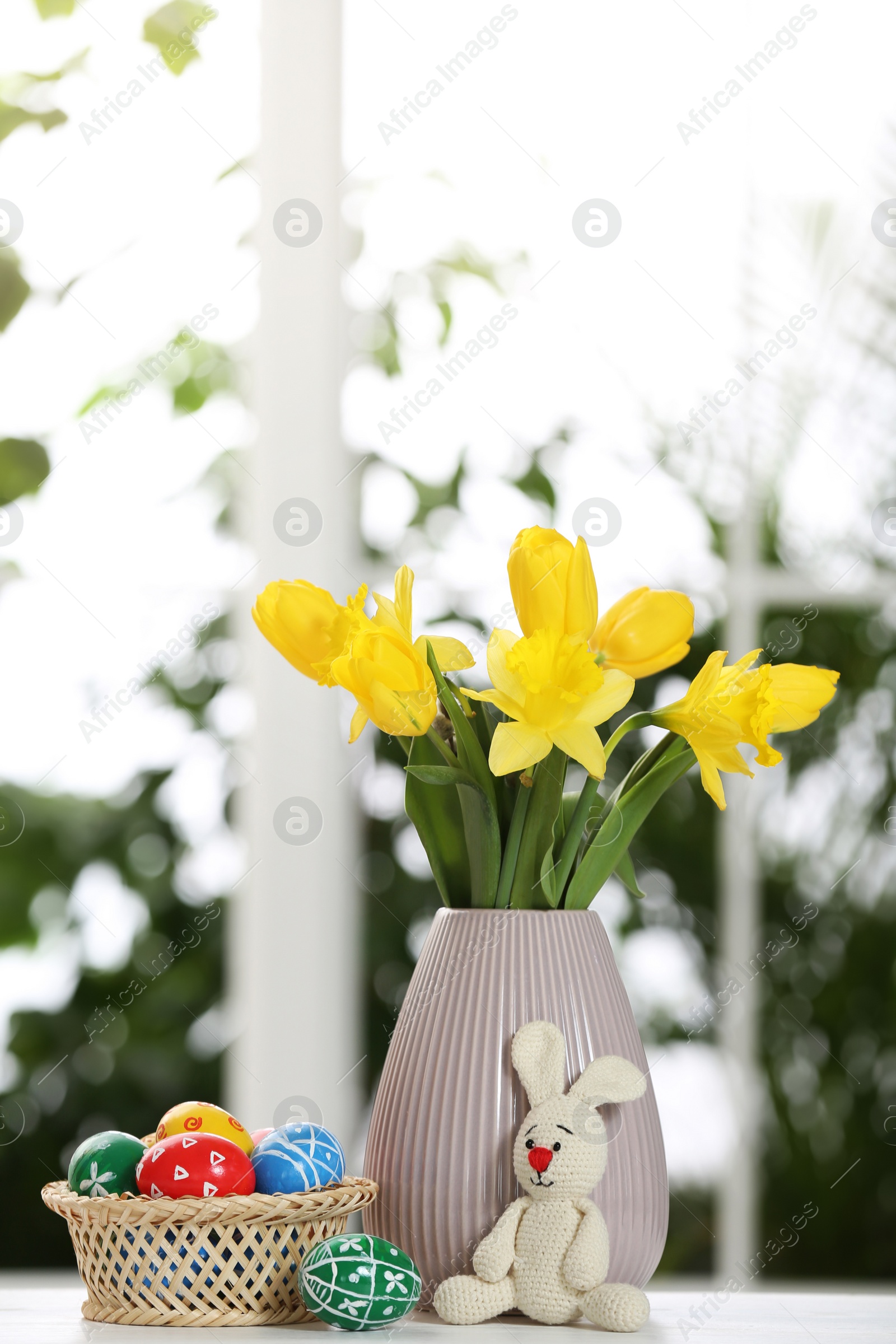 Photo of Festive composition with Easter eggs on table against blurred window