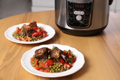 Photo of Plates with meat and garnish prepared in multi cooker on wooden table