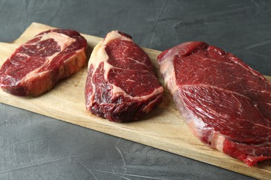 Wooden board with pieces of raw beef meat on grey table