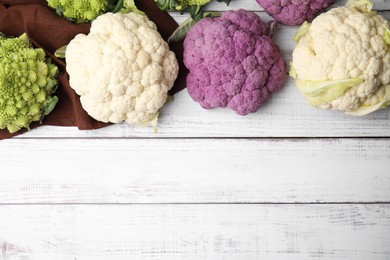 Different fresh cabbages on white wooden table, flat lay. Space for text