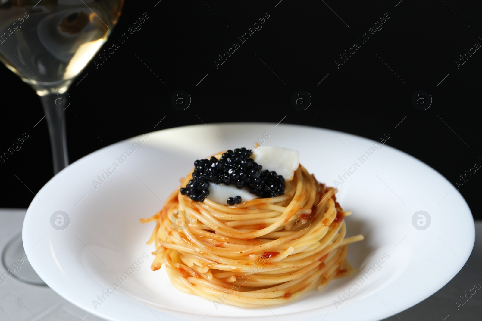 Photo of Tasty spaghetti with tomato sauce and black caviar on plate against dark background, closeup. Exquisite presentation of pasta dish