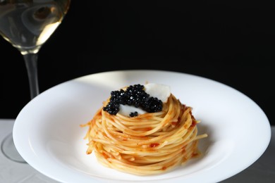 Tasty spaghetti with tomato sauce and black caviar on plate against dark background, closeup. Exquisite presentation of pasta dish