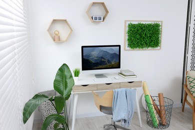 Green artificial plant wall panel and desk with computer in light room. Interior design