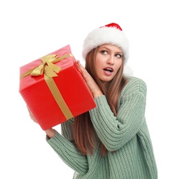 Emotional young woman in Santa hat with Christmas gift on white background