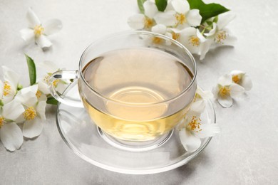 Photo of Glass cup of jasmine tea and fresh flowers on grey table