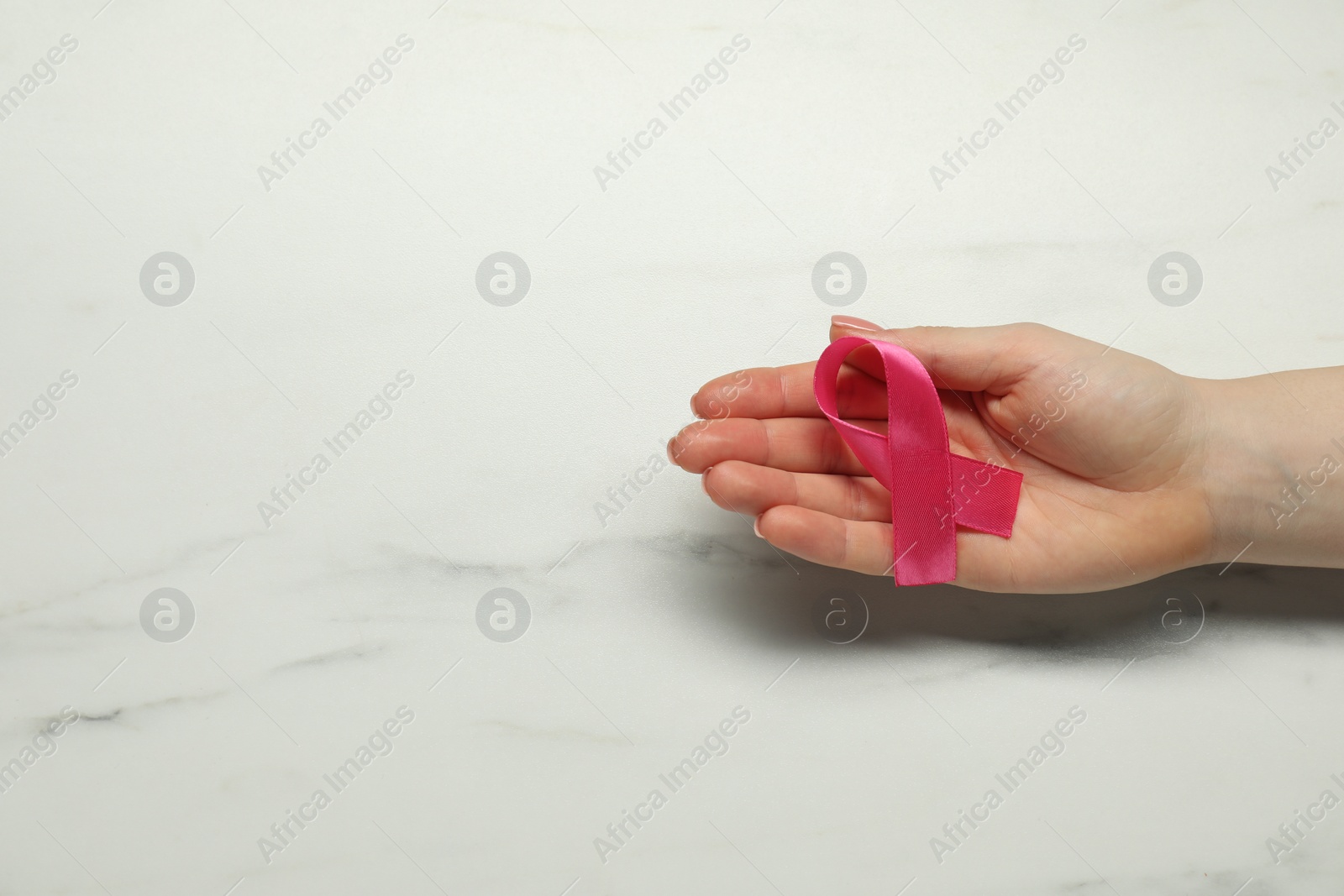 Photo of Breast cancer awareness. Woman with pink ribbon at white marble table, top view. Space for text