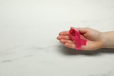 Breast cancer awareness. Woman with pink ribbon at white marble table, top view. Space for text
