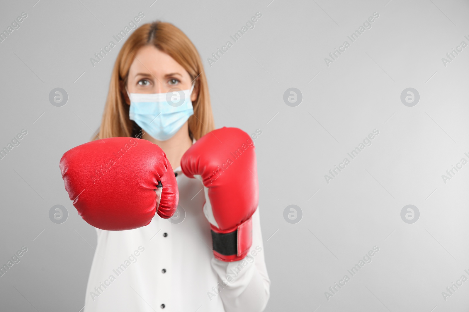 Photo of Woman with protective mask and boxing gloves on light grey background, space for text. Strong immunity concept