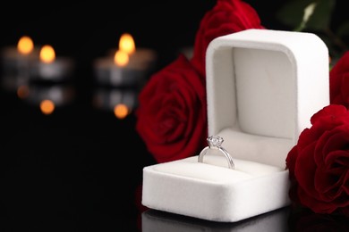 Photo of Beautiful engagement ring with gemstone in box and roses on black background. Space for text