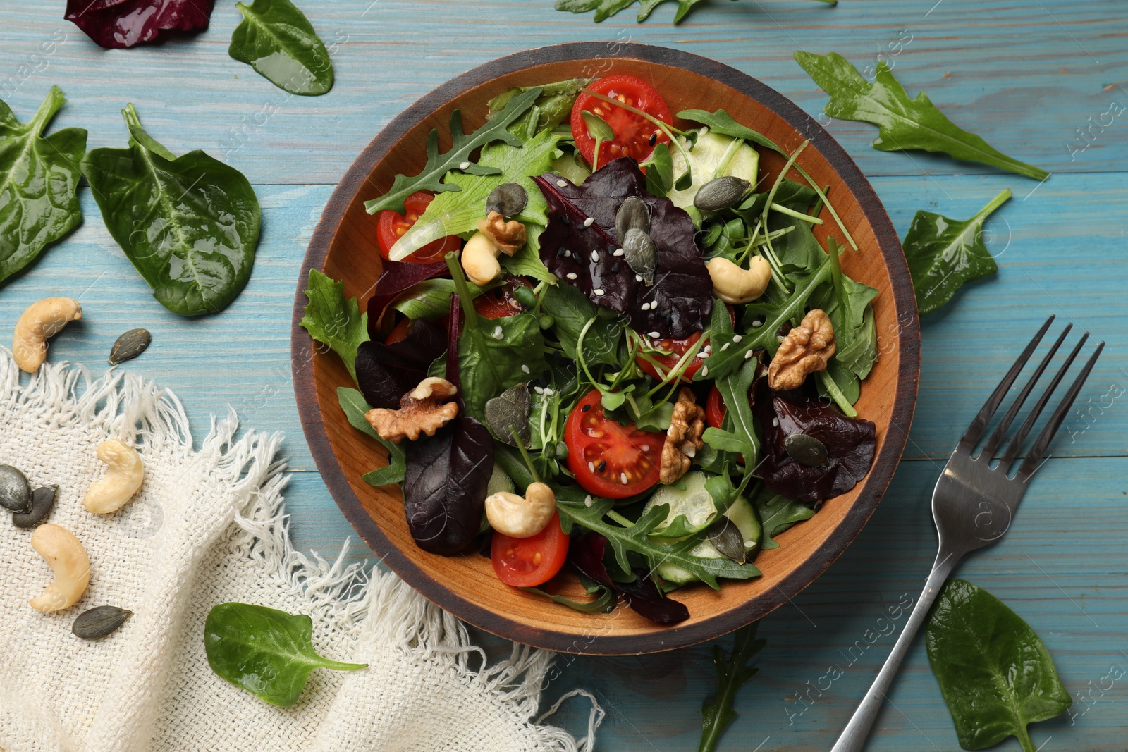 Photo of Tasty fresh vegetarian salad and fork on light blue wooden table, top view