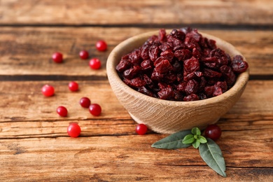 Photo of Tasty fresh and dried cranberries with leaves on wooden table