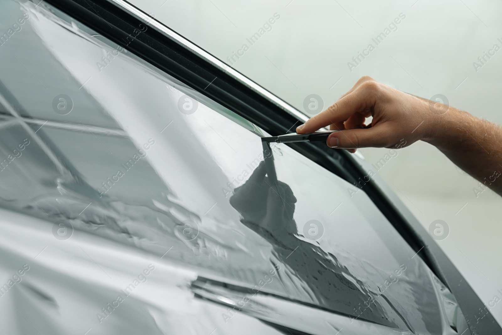 Photo of Worker tinting car window with foil in workshop, closeup