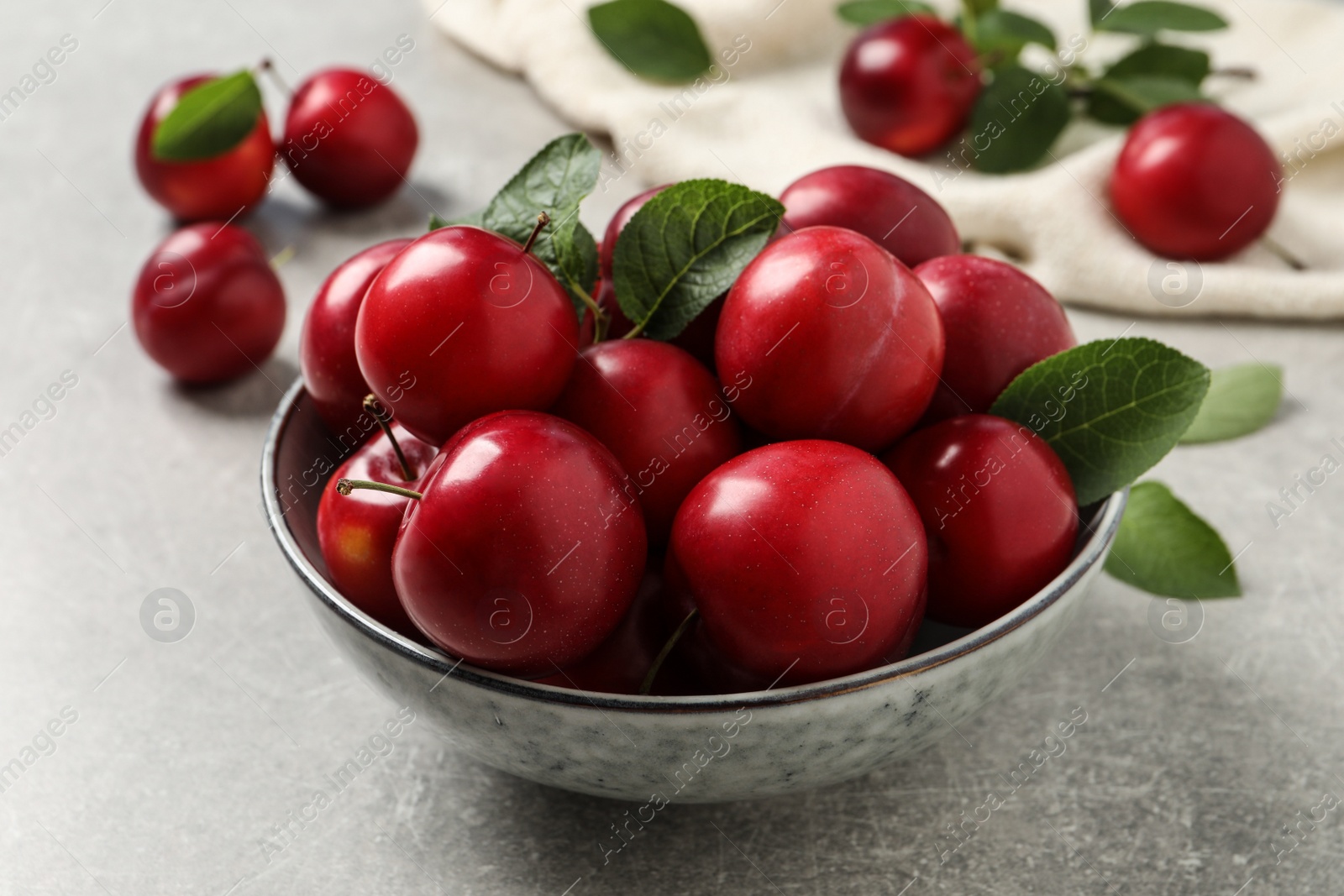 Photo of Delicious ripe cherry plums with leaves on light table