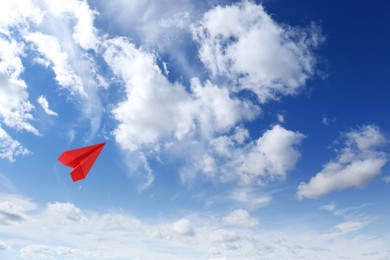 Image of Red paper plane flying in blue sky with clouds