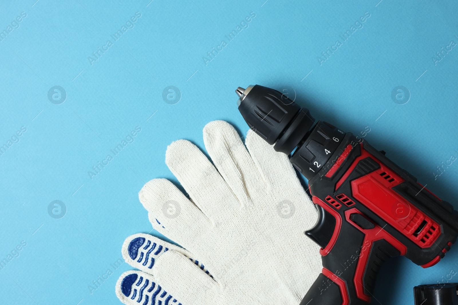 Photo of Electric screwdriver and gloves on light blue background, top view. Space for text