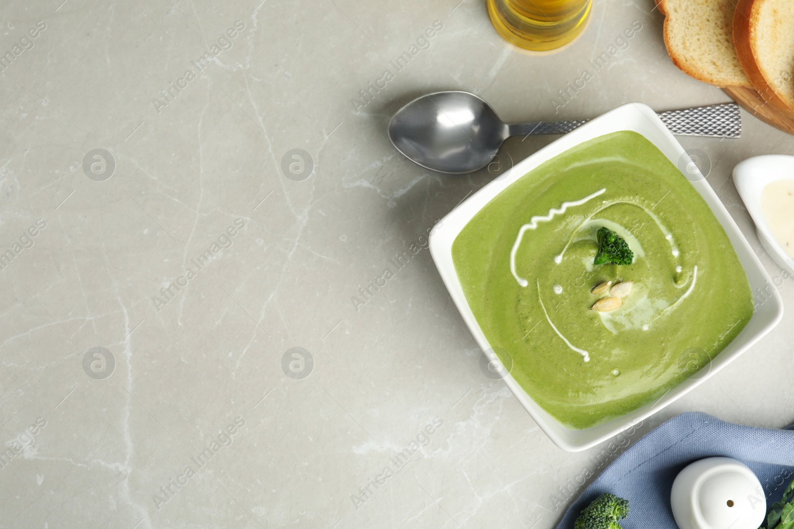 Photo of Delicious broccoli cream soup served on grey marble table, flat lay. Space for text