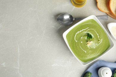 Delicious broccoli cream soup served on grey marble table, flat lay. Space for text