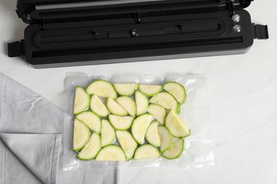 Photo of Sealer for vacuum packing with plastic bag of zucchini on white table, flat lay