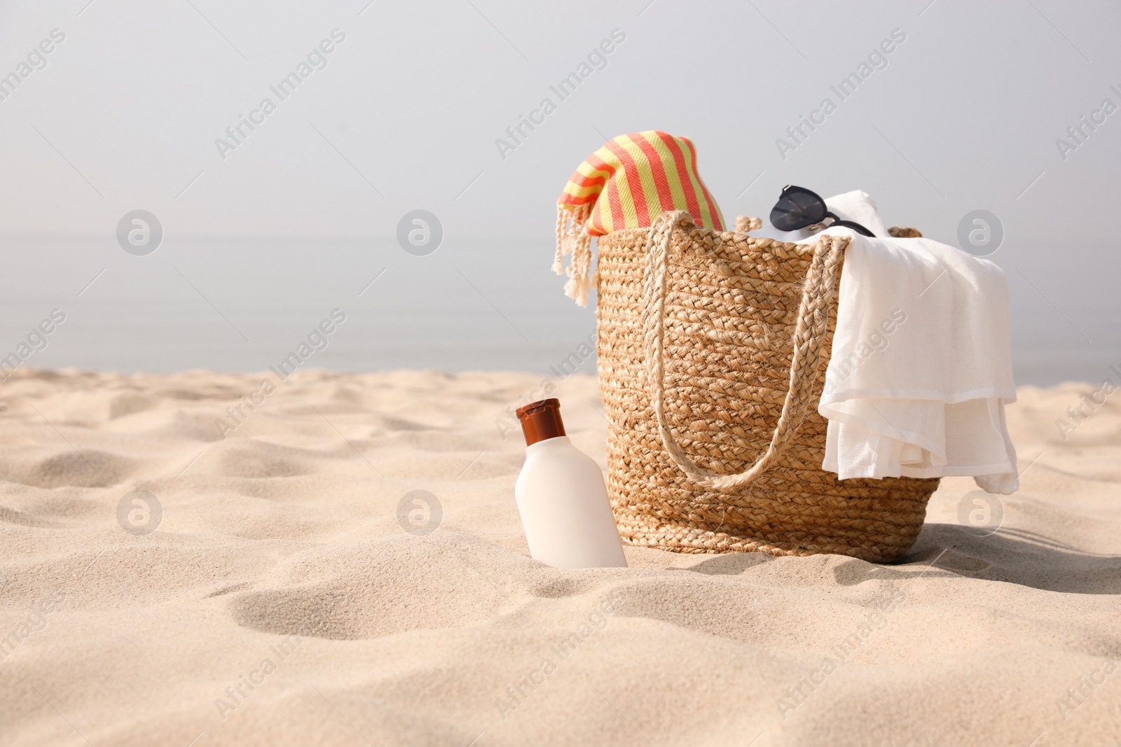 Photo of Beach bag, towel, blanket, sunglasses and sunscreen on sandy seashore, space for text