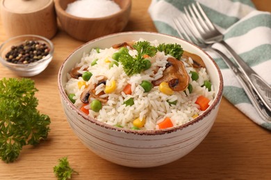 Bowl of delicious rice with vegetables on wooden table, closeup