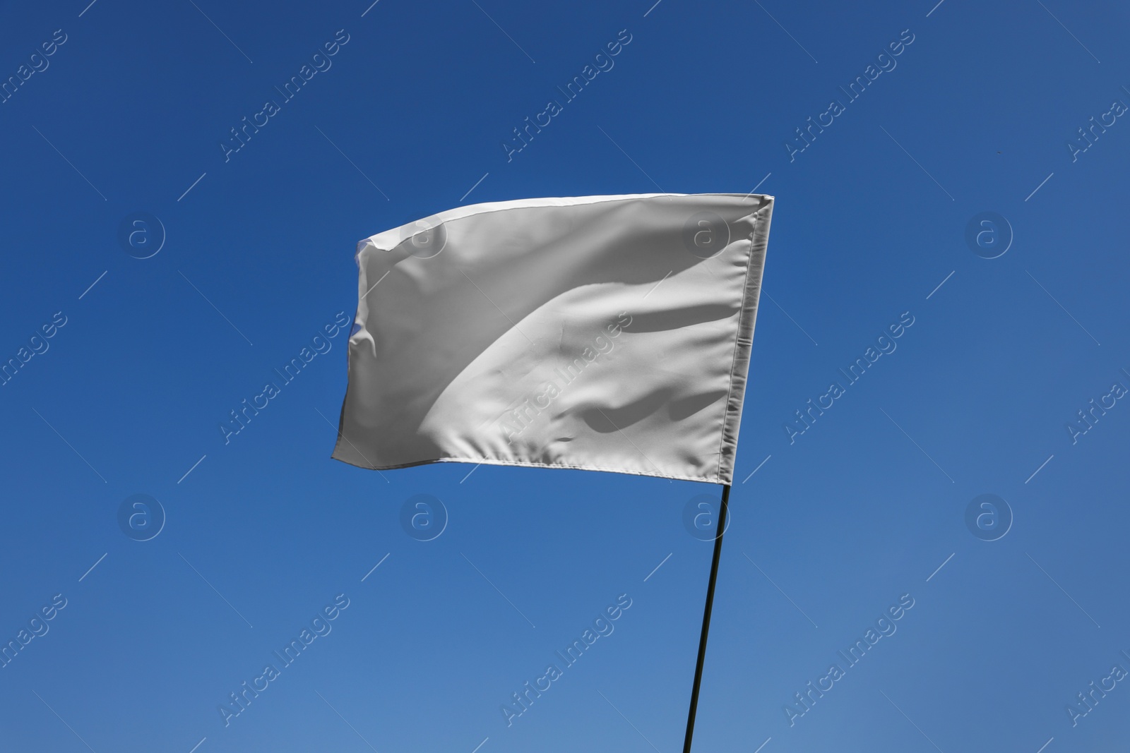 Photo of White flag fluttering against blue sky on sunny day