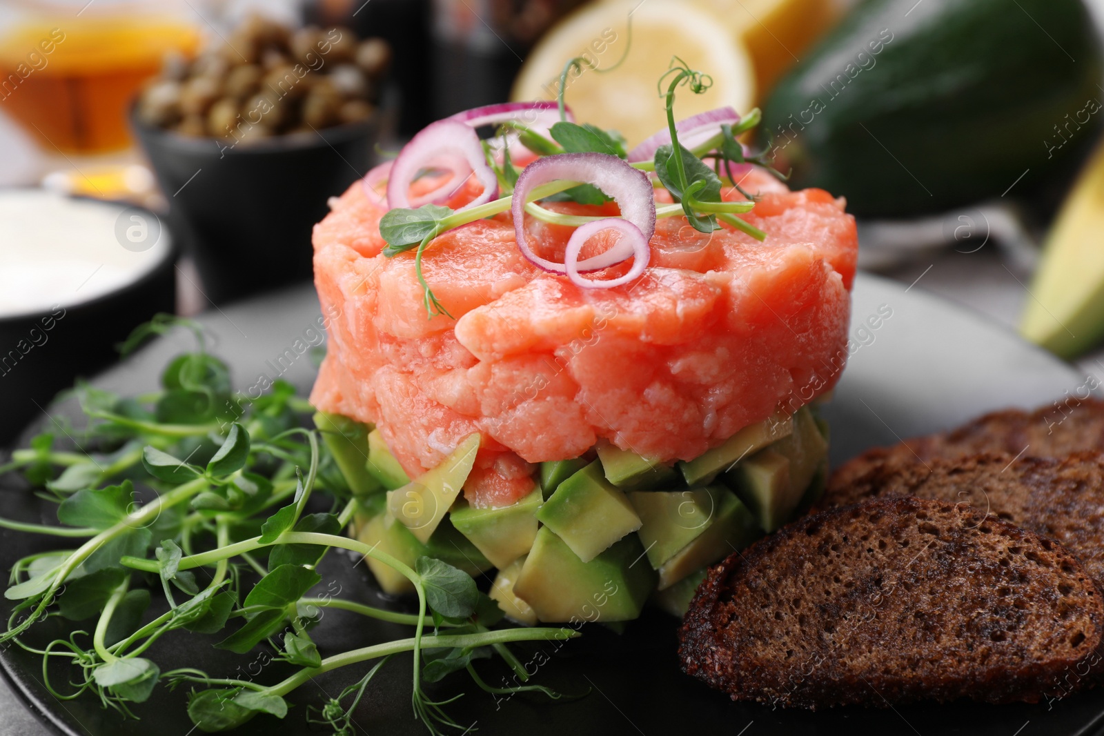 Photo of Tasty salmon tartare with avocado, microgreens and croutons on plate, closeup