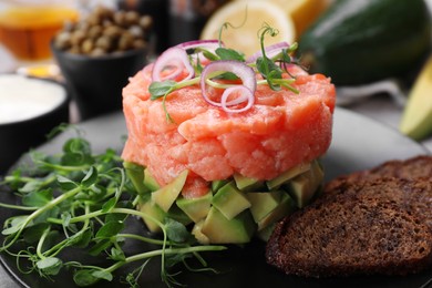 Tasty salmon tartare with avocado, microgreens and croutons on plate, closeup