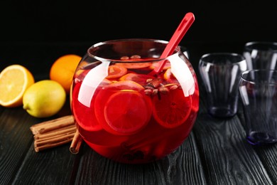 Photo of Bowl of delicious aromatic punch drink, ingredients and empty glasses on black wooden table