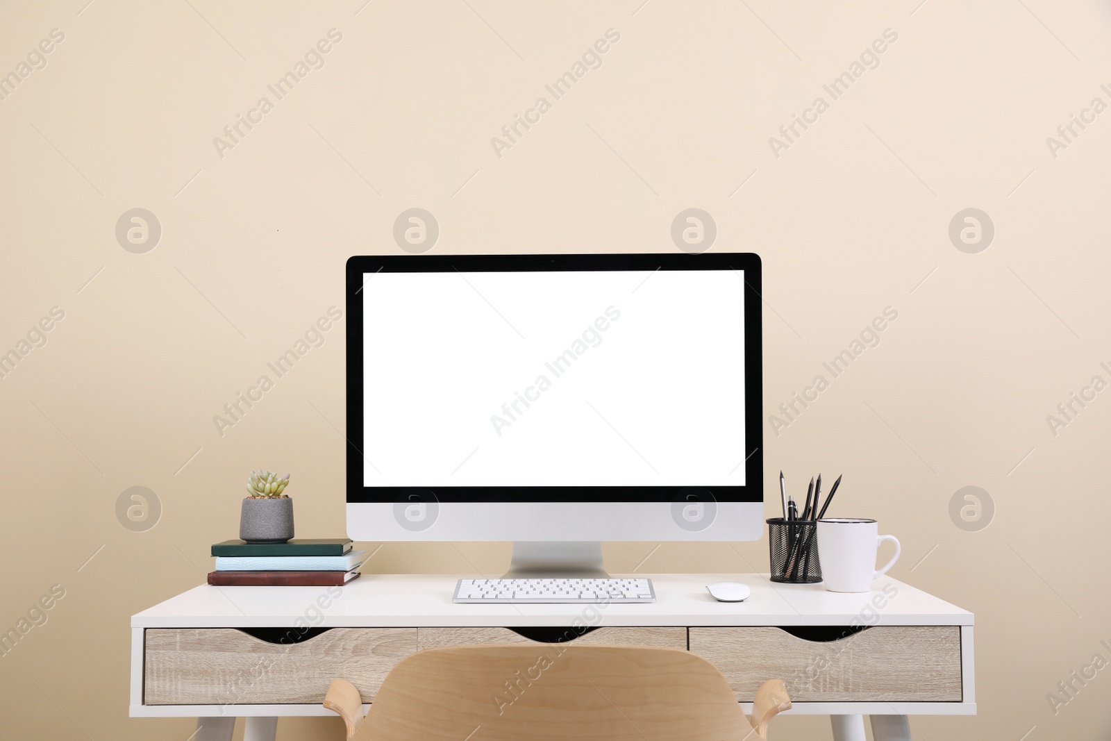 Photo of Comfortable workplace with blank computer display on desk near beige wall. Space for text