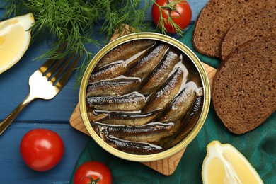 Tin can with tasty sprats served on blue wooden table, flat lay