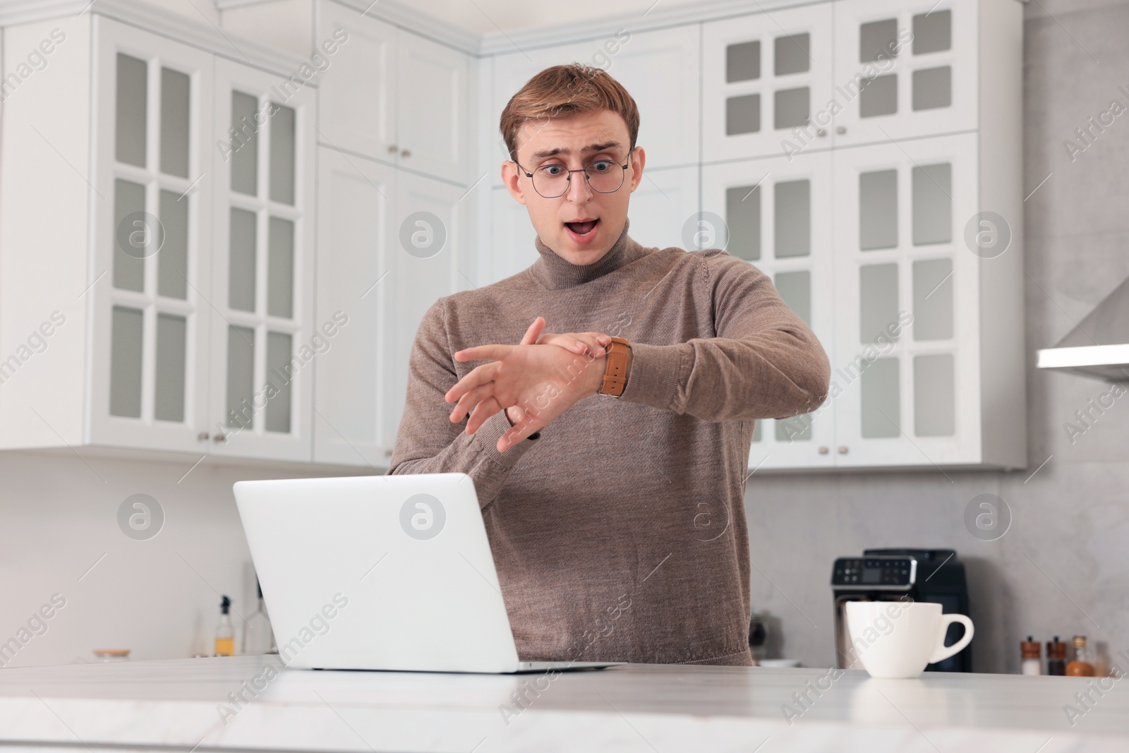 Photo of Emotional young man checking time in kitchen. Being late