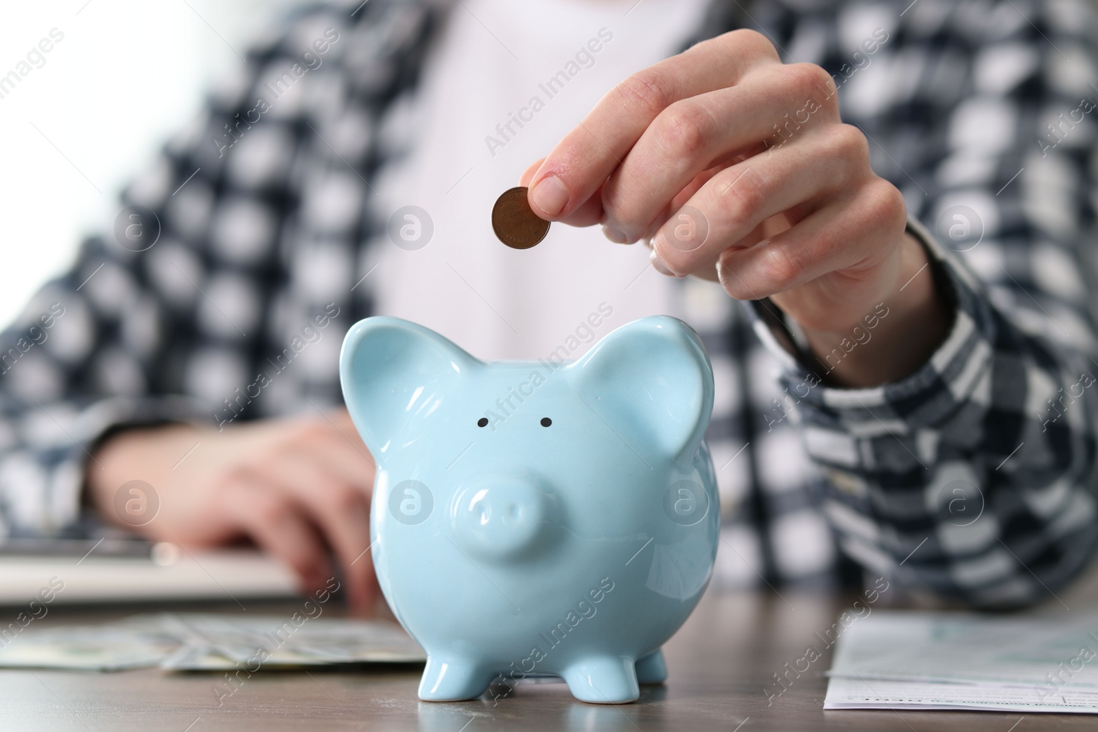 Photo of Financial savings. Man putting coin into piggy bank at wooden table, closeup