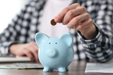 Photo of Financial savings. Man putting coin into piggy bank at wooden table, closeup