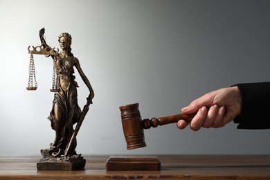 Photo of Judge striking mallet at wooden table against grey background, closeup. Figure of Lady Justice indoors