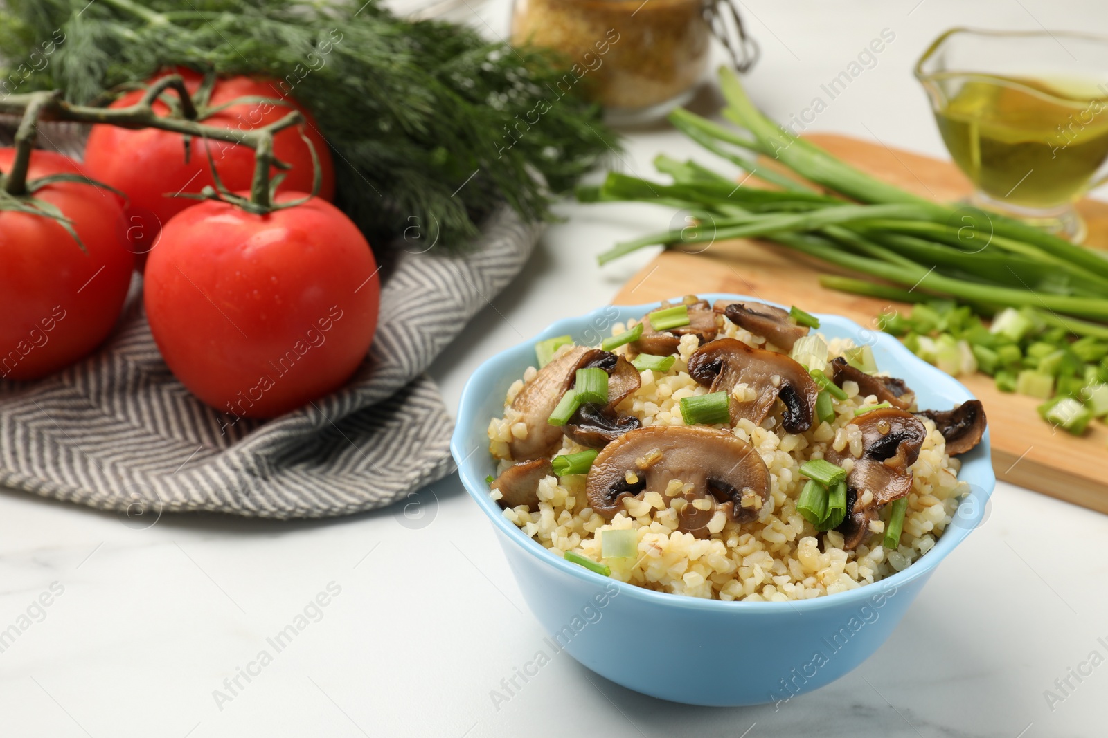 Photo of Delicious bulgur with mushrooms, green onion and other products on white table, closeup