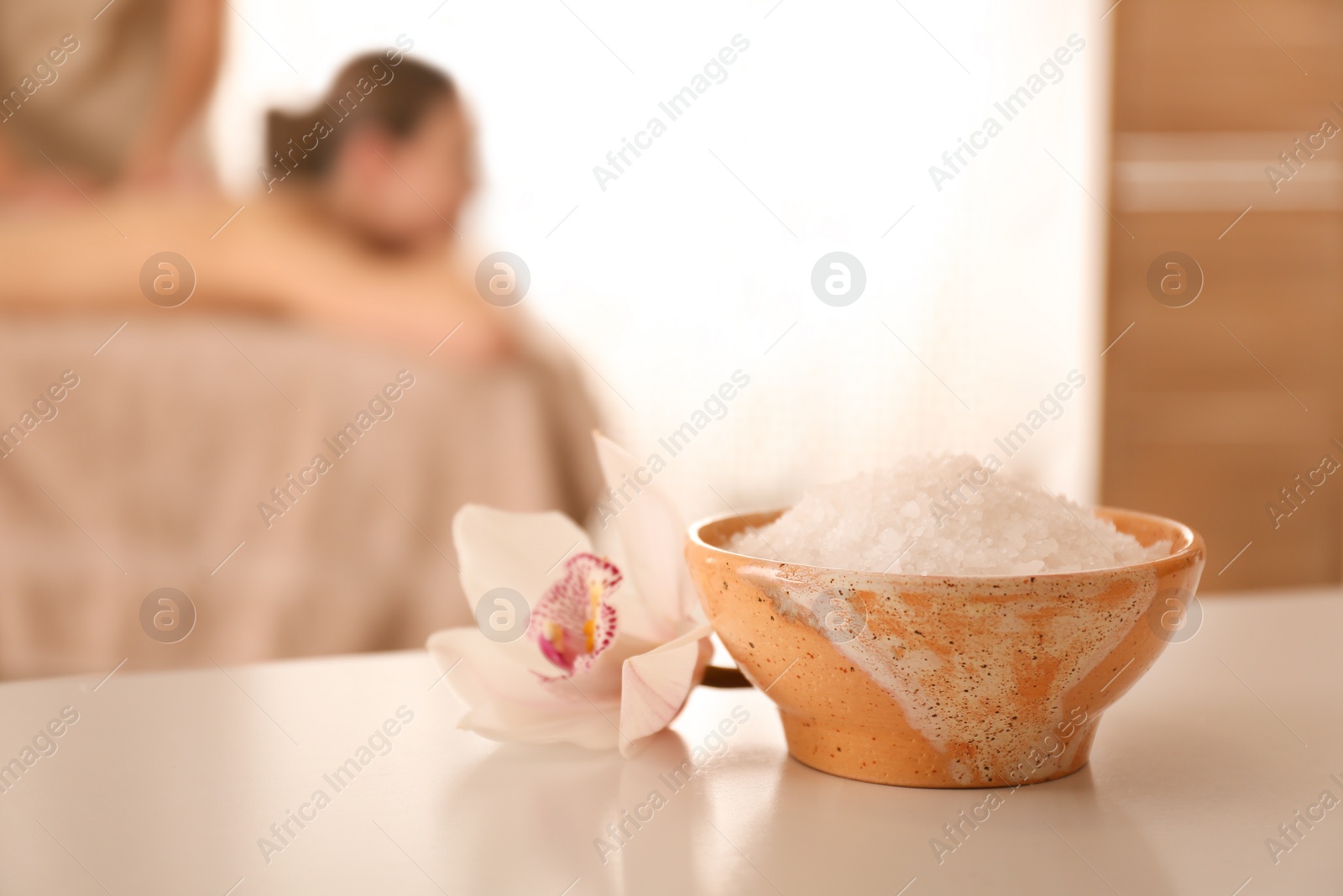 Photo of Bowl with sea salt and orchid flower on white table in spa salon. Space for text