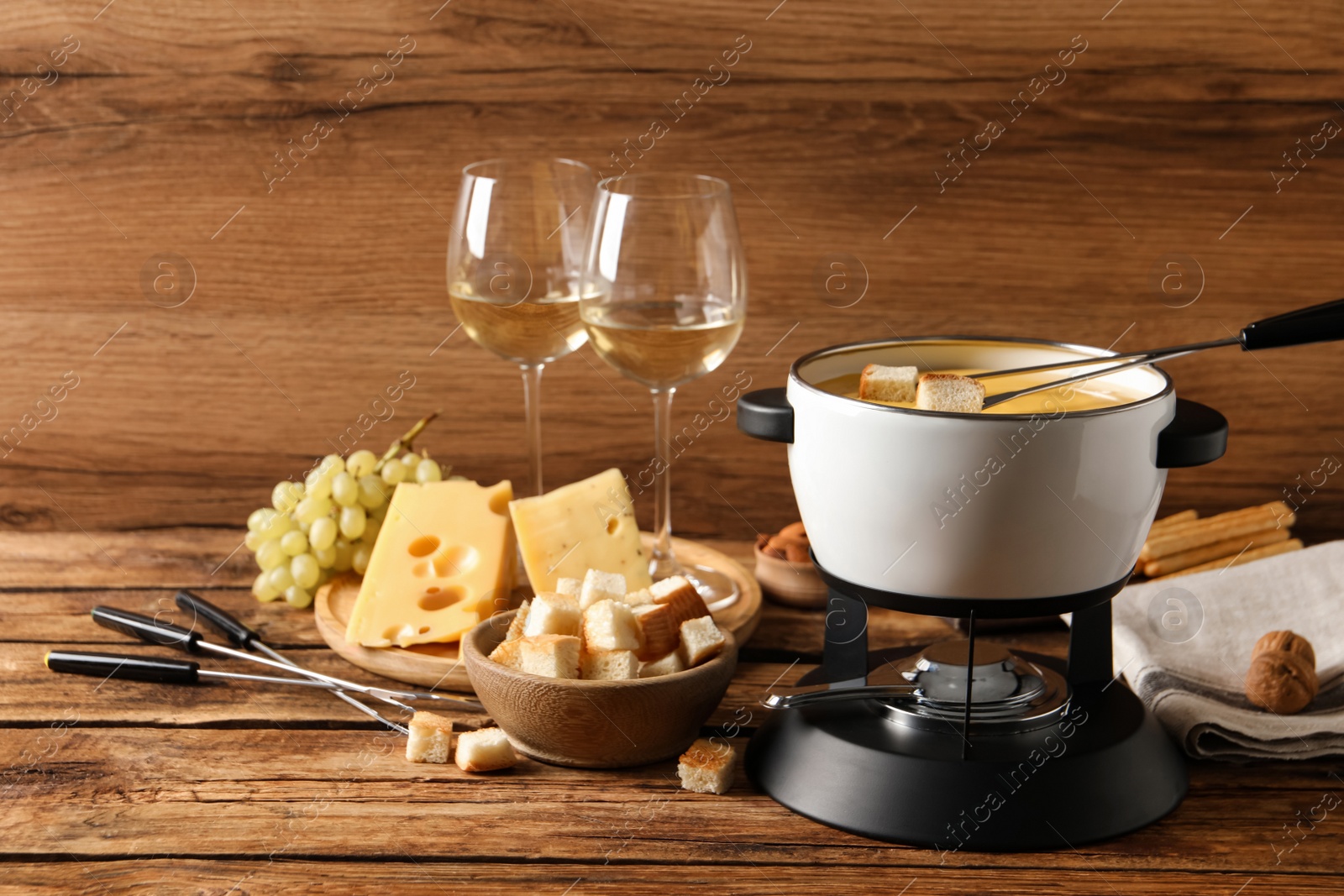 Photo of Pot of tasty cheese fondue, snacks and wine on wooden table